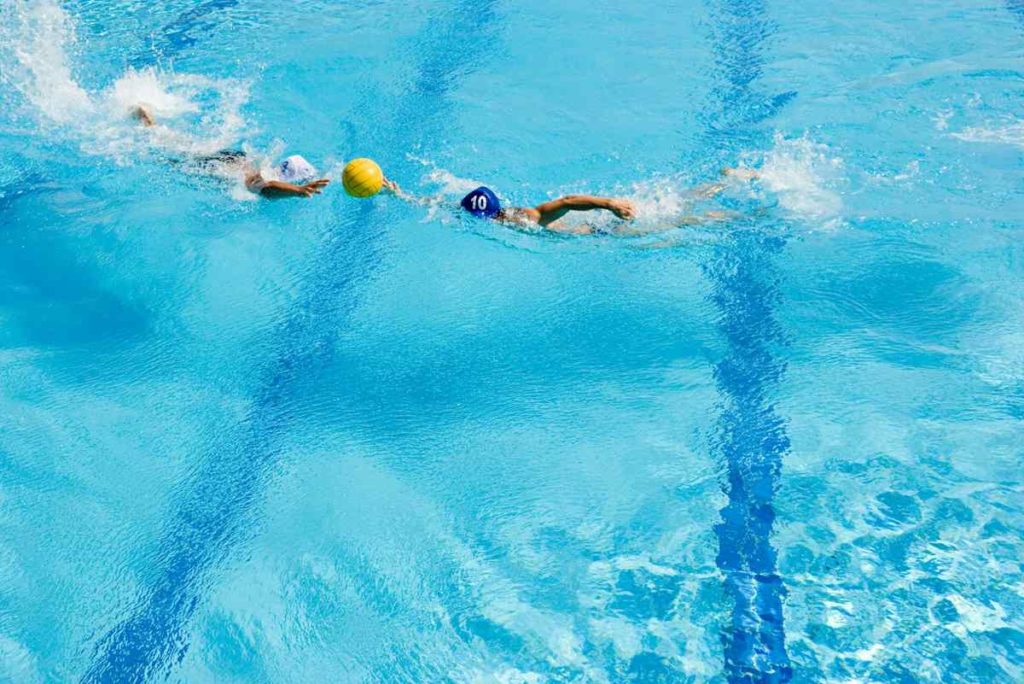 Deux sportifs nagent pour attraper un ballon jaune en premier.