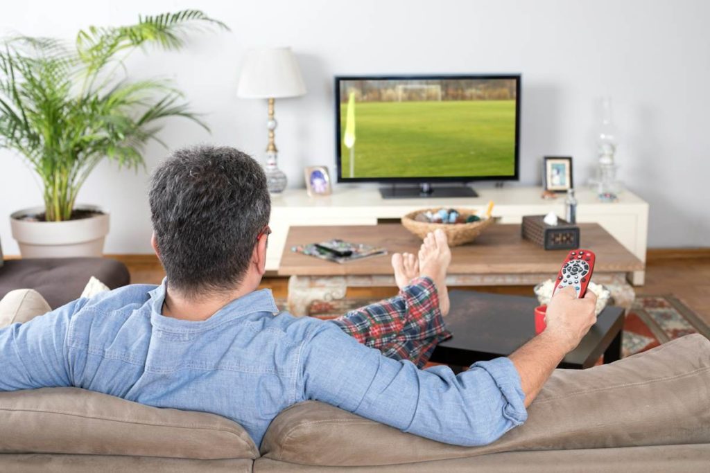 Un téléspectateur assis dans un canapé, regarde un match à la télé.