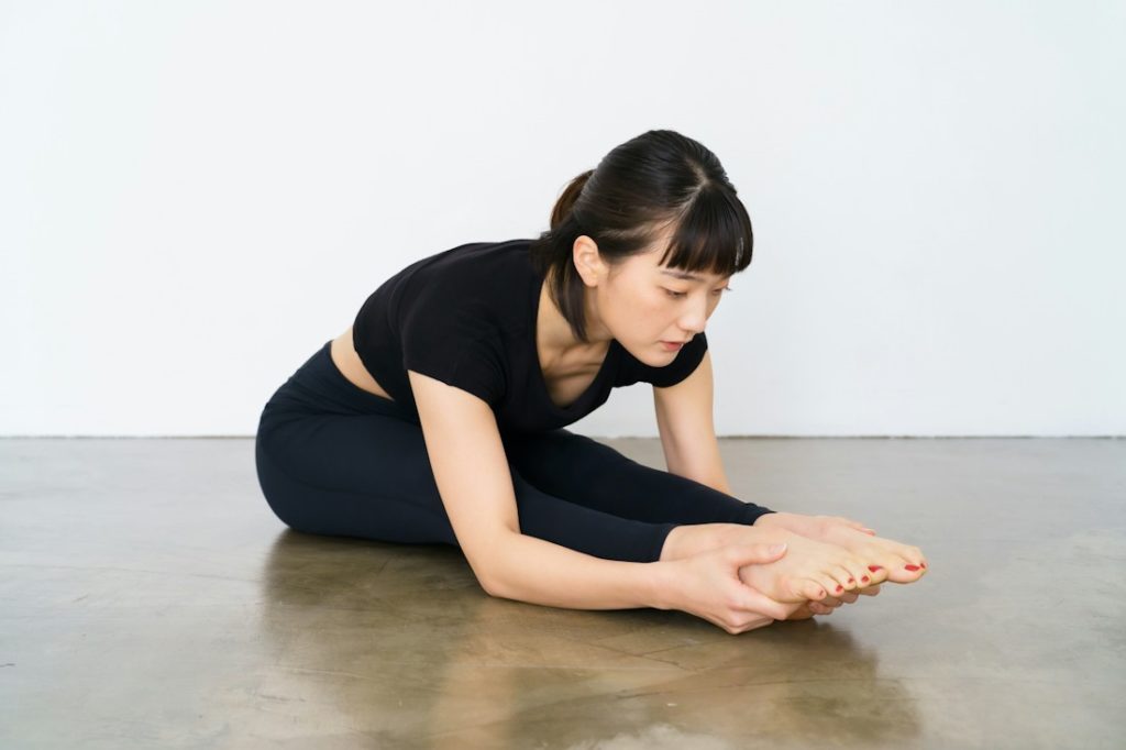 Une sportive fait une figure de yoga avec les jambes tendues au sol.