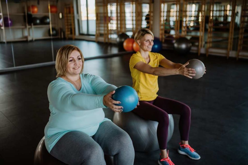 Une femme en surpoids fait du sport en salle avec une professeur.