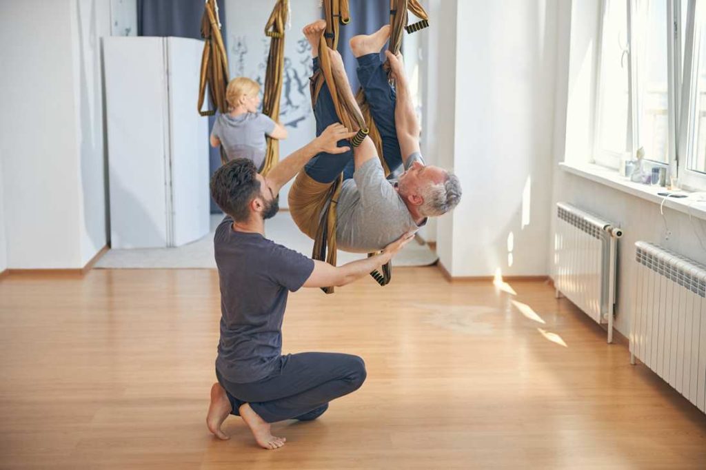 Un homme accompagne un retraité dans son exercice physique dans une pièce lumineuse.