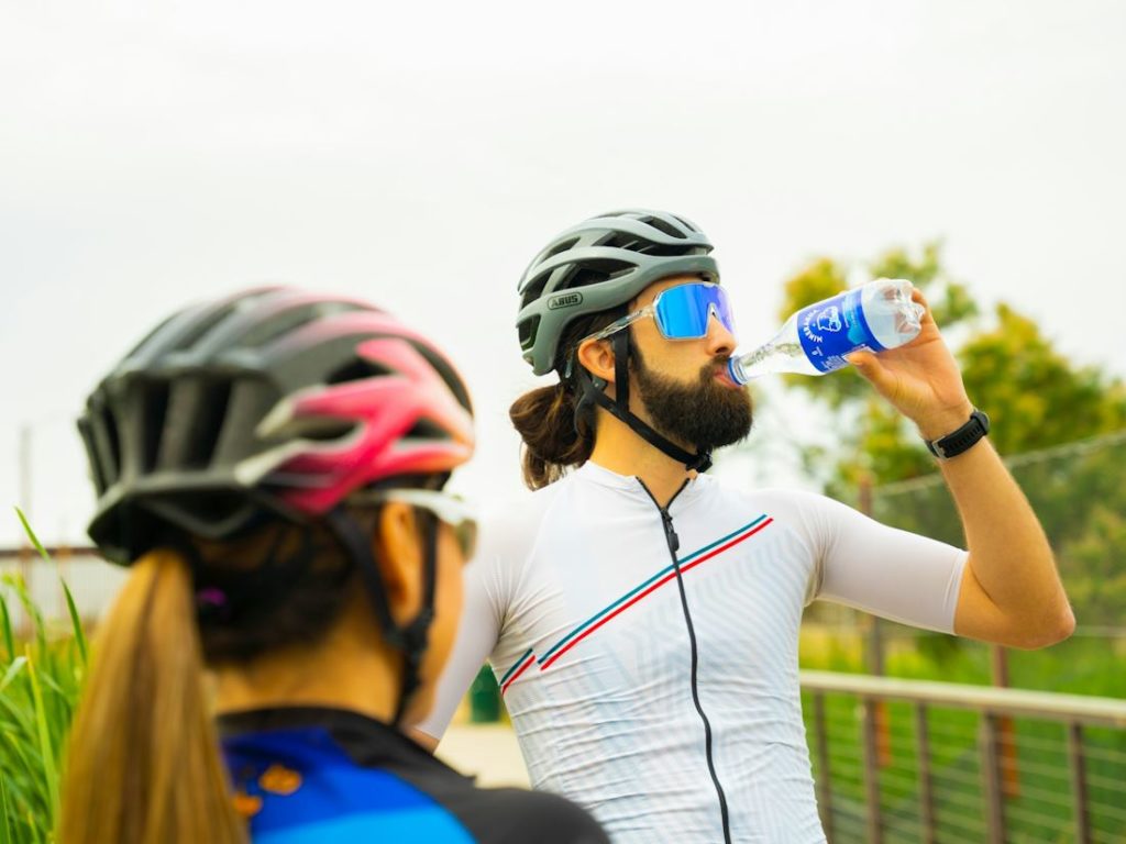 Deux personnes avec un casque de vélo sur la tête dont l'un est en train de boire.