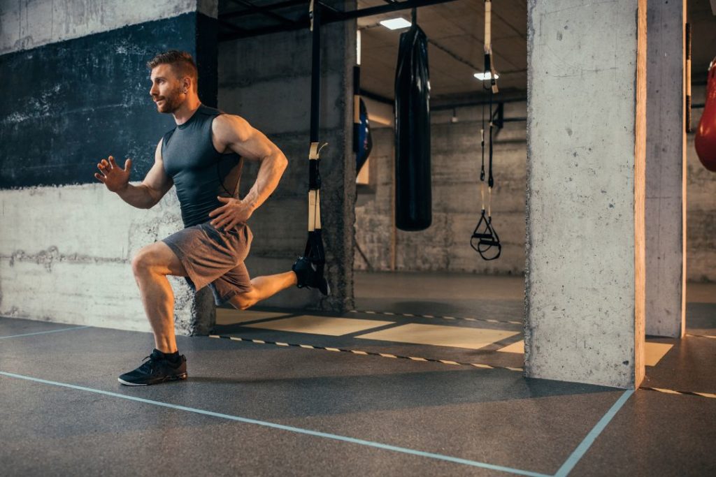 Un homme en train de faire des fentes en salle de sport.