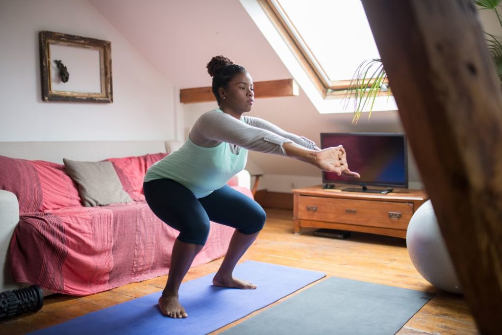 Une femme en train de faire des squats chez elle.