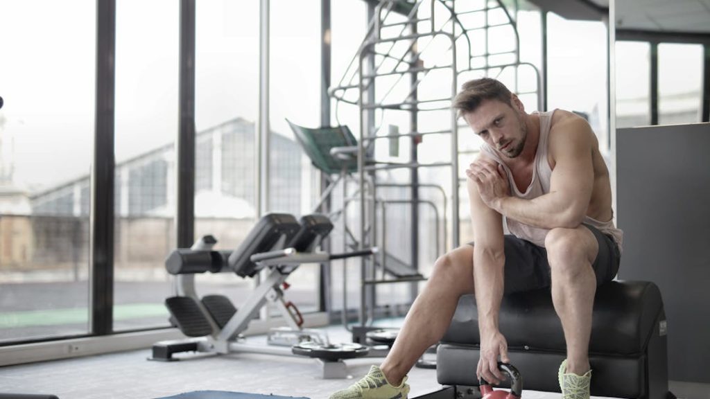 Un sportif se tient l'épaule droite avec la main gauche, dans une salle de sport.