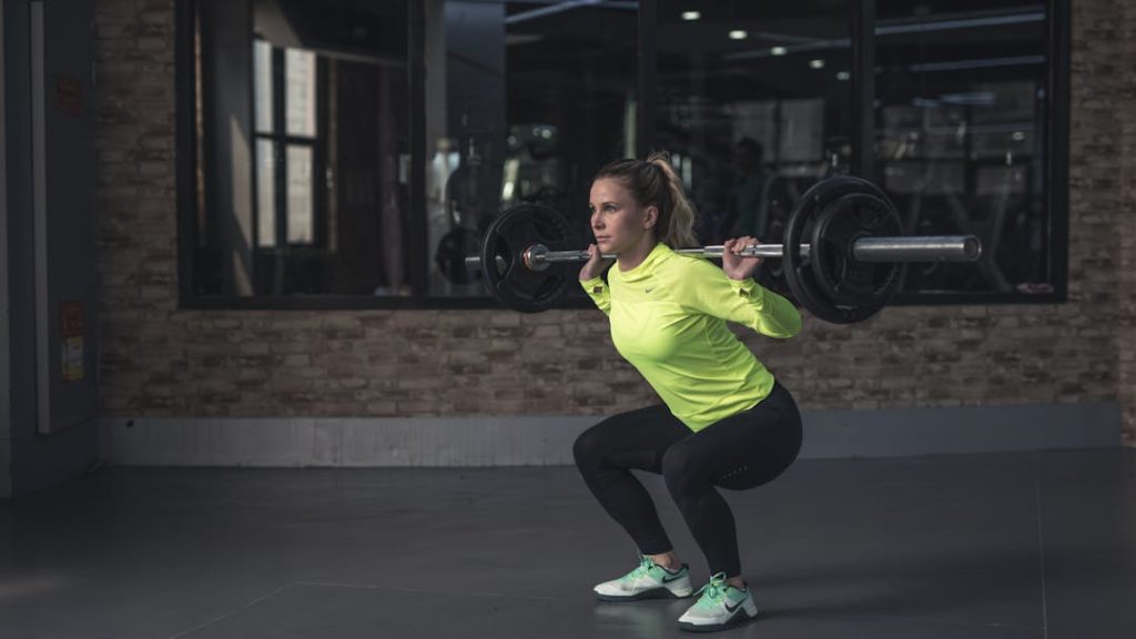 Vue d'une femme vêtue de jaune et d'un leggin noir, en train de faire un squat dans une salle de sport.