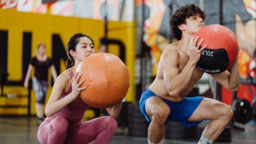 Deux personnes en train de faire des squats avec un ballon à la main.