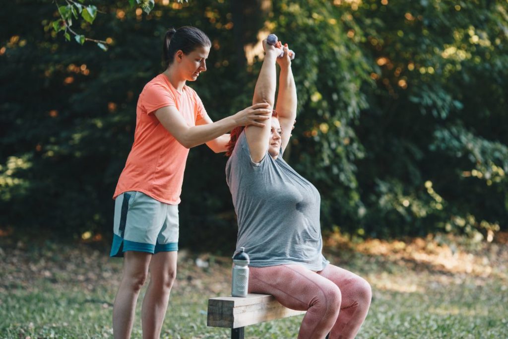 Une femme et sa coach en train de faire des étirements dans un parc.