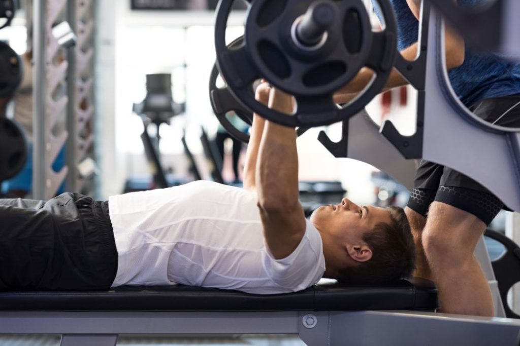 Un sportif se fait accompagner par un coach personnel sur une machine de musculation.