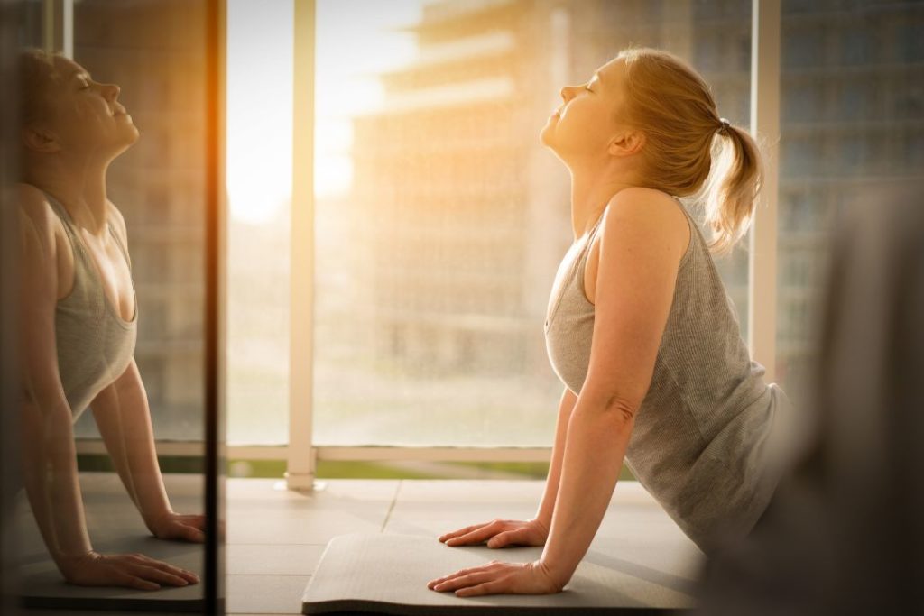 Une femme vue de profil, en train de faire une posture de yoga.