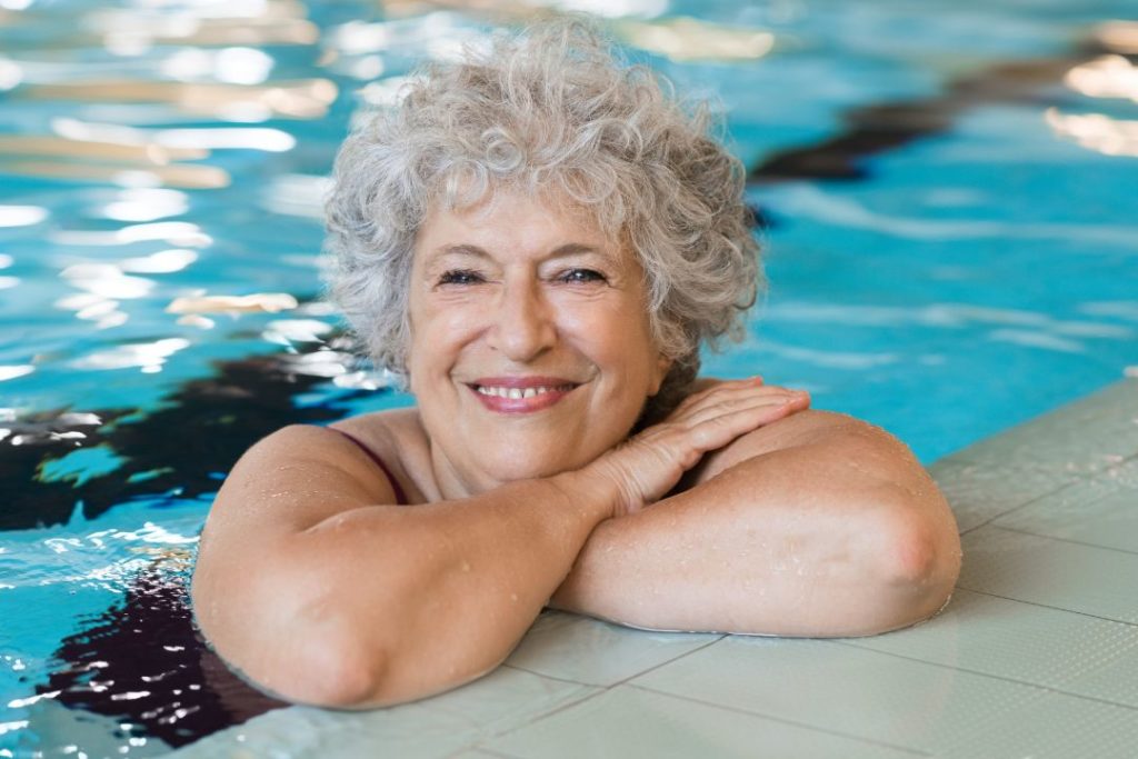 Une dame âgée accoudée au bord d'une piscine municipale.