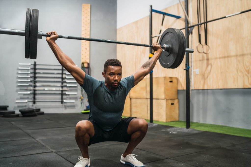 Homme en overhead squat avec barre dans une box de CrossFit.